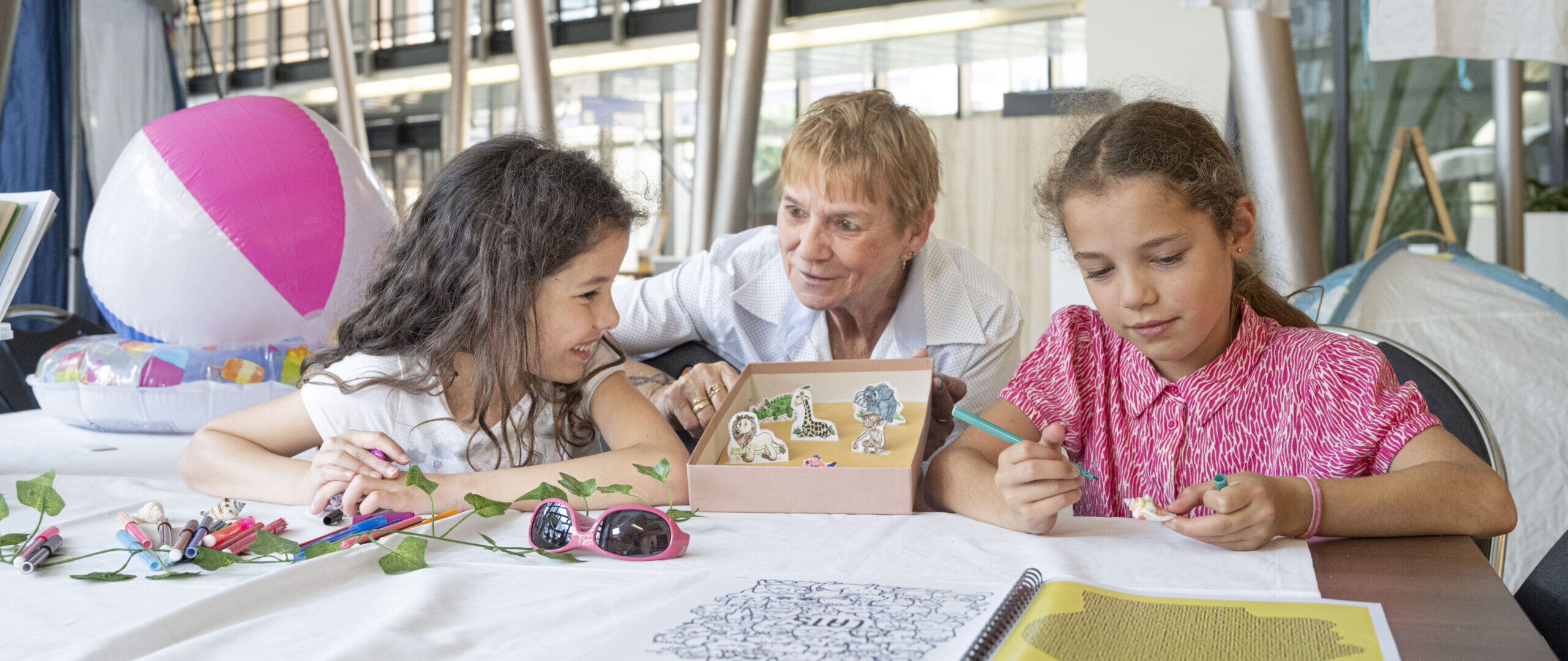 Twee kinderen knutselen samen met een begeleider op de WKZ-camping in de centrale hal van het Wilhelmina Kinderziekenhuis.